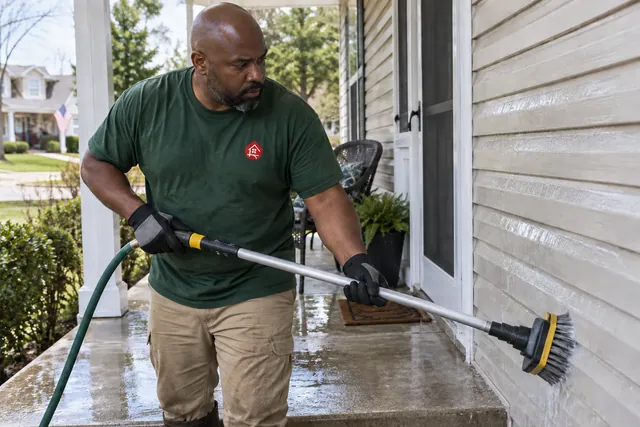 Worker washing a low porch and siding with a hose brush attachment